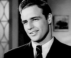 Celebrity gif. A young Marlon Brando rolls his eyes and then smirks knowingly.