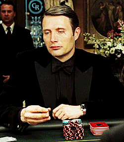 Movie gif. Mads Mikkelsen as
 Le Chiffre in Casino Royale. He sits at a poker table and plays with his chips in his hand as the other hand is on his temple and he stares unblinkingly at Bond, who is across from him.