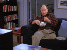 Seinfeld gif. Jason Alexander as George sits on a couch with a bowl of popcorn and munches while watching the TV.