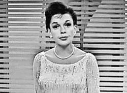Celebrity gif. Judy Garland shrugs her shoulders and raises her eyebrows while cocking her head as she considers.