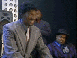TV gif. On Chappelle’s Show, a suited-up Dave Chappelle doubles over laughing hysterically, slapping his hand on his knee and grasping the hand of Charlie Murphy who begins to laugh along.