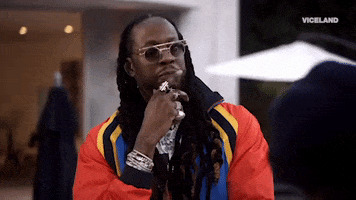 Reality TV gif. Wearing sunglasses, 2 Chainz ponders something, holding a finger up to his chin.