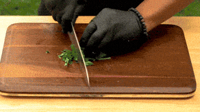 Close-up of hands chopping fresh herbs on a wooden board while preparing a home-cooked recipe