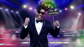 Video gif. A man is in front of a disco party green screen and he shakes his head back and forth, dancing while holding a sign that says, "It's party time!"