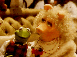 Muppets gif. Kermit and Miss Piggy, dressed-up in holiday finery, lean their heads together affectionately.
