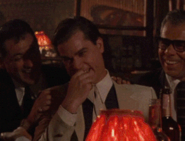 Movie gif. Ray Liotta as Henry in Goodfellas stands and laughs with others. He rubs his face and buckles over in laughter. 