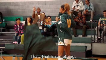TV gif. A woman wearing a basketball uniform in Grownish takes off her jacket as a man standing in the bleachers points toward and says, "That. That is something."