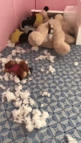 Video gif. Gigantic teddy bear, with stuffing ripped out onto the floor, appears to be rolling around on its own until we notice a small dog or cat is stuck in the bear's crotch, its tail sticking out as it tries to escape and the bear continues thrashing.