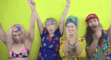 Celebrity gif. Dressed in tropical-print clothes, four members of Tacocat celebrate, clapping and cheering and raising their arms victoriously.