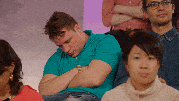Video gif. We see a studio audience with tiered seating, where almost everyone is applauding, but a man in a teal polo shirt is asleep. He wakes up, a bit disoriented, and starts clapping without understanding why.