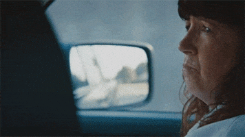 TV gif. Ann Dowd as Patti in Leftovers sits in the passenger seat of a car as it drives. She keeps her fingers crossed and looks at the driver.
