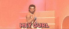 Video gif. We zoom in on a man wearing a gold lamè headband and spandex tank top as he looks over his shoulder at us with an intense gaze. Text, "Hey gurl."