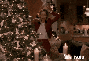 TV gif. Calista Flockhart, as Ally in Ally McBeal does a goofy dance in front of a Christmas tree as she holds a star on top of her head.