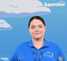 Celebrity gif. Lauren Ash is in her blue Cloud9 polo shirt on the set of Superstore. She gives us a friendly wave.