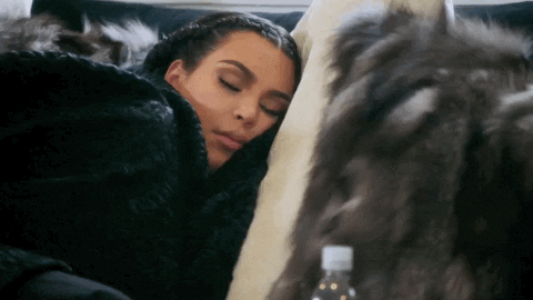 Celebrity gif. Kim Kardashian is bundled up in blankets, sleeping peacefully on a couch.