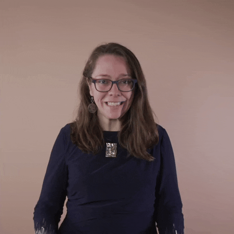 Reaction gif. A Disabled Latina woman with brown wavy hair and glasses tightens her muscles, fists positioned as if grasping something in front of her, and shakes them vigorously with an enigmatic grin.