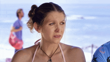 Video gif. A woman on the beach gives a nervous side eye to someone off screen, looking very uncomfortable or scared. 