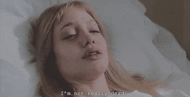 Movie gif. Angelina Jolie as Lisa in Girl, Interrupted. She's laying in a hospital bed and looks very ill and she softly says, "I'm not really dead."
