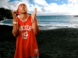 Celebrity gif. LL Cool J is standing in front of a beach with a jersey on and he puts his hands in the prayer position as he leans upwards towards the sky, wishing with all his might.