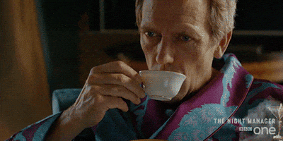 TV gif. Wearing a robe, Hugh Laurie, as Richard in The Night Manager takes a sip of tea, then closes his eyes in pleasure as he swallows.