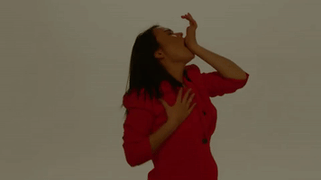 Celebrity gif. Mitski in a red coat holds her palm to her mouth as her other hand moves up her chest to her neck with eyes closed, gasping as she mimics a passionate gesture.