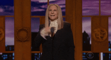 Celebrity gif. Barbara Streisand is presenting at the Tony Awards and she raises a hand up to the crowd while looking elated.