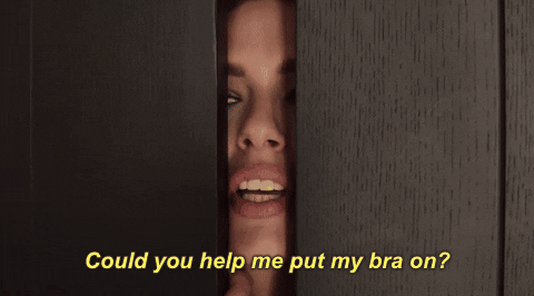 Gif of a woman peeking through the gap in a door saying "could you help me put my bra on?"