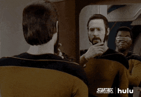 TV gif. Brent Spiner as Data and Michael Dorn as Worf in Star Trek: The Next Generation. They're both staring at the mirror at Data'a reflection, considering how they feel about his new beard, which he strokes.