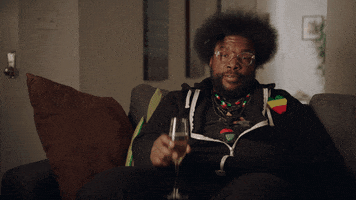 TV gif. Sitting on a couch, on Drunk History, Questlove raises his glass toward us to cheers.