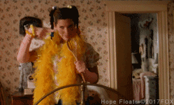 Movie gif. Sandra Bullock as Birdie in "Hope "Floats wears a yellow feather boa as she dances in a bedroom in a dramatic over-the-top way.