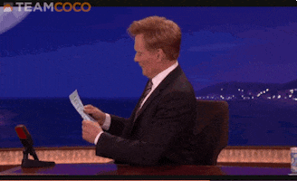 Celebrity gif. Talk show host Conan O'Brien looks up from a sheet of paper and pretends like he's shocked to see us. He turns to face us and sets the paper down, saying, "Oh, hello there!"