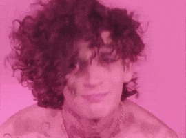 Music video gif. From the 1975's "Love Me," Matthew Healy is bathed in pink light as he nods his head rapidly and says yeah.