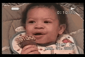 Video gif. In a home video dated March 31, 2007, a young baby grasps a Drumstick ice cream cone with a serious expression before bursting into laughter.