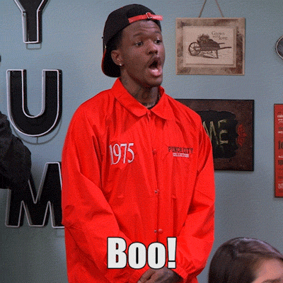 Video gif. A young man in a bright red jumpsuit and a backwards hat, his hands clasped in front of him, yells, "Boo," text which also appears on the screen.