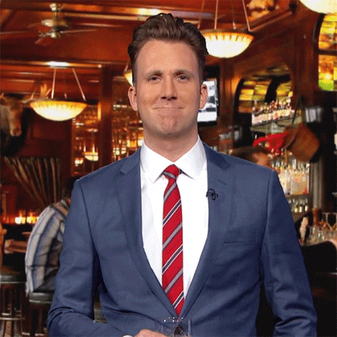 TV gif. Dressed in a suit in a pub, Jordan Klepper bows his head and raises his beer to cheers us.