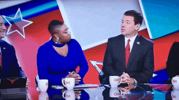 Political gif. Symone D. Sanders on a CNN panel looks shocked at what the man next to her is saying, so she waves him off and picks up her phone.