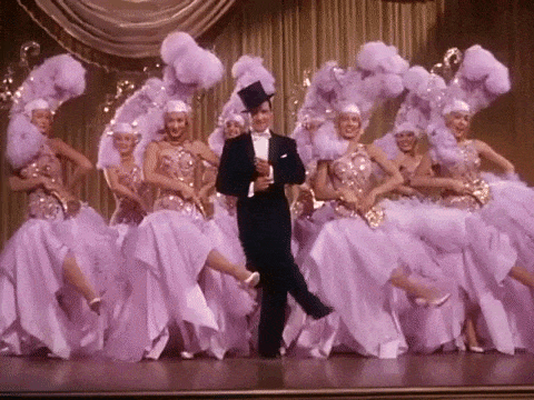 Women dressed in fancy clothes dance around a man.