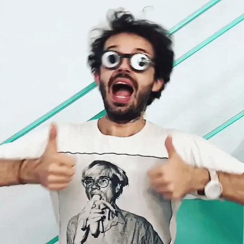 Video gif. Man with googly eye goggles gives us a double thumbs up and shakes his face and body with mouth open.
