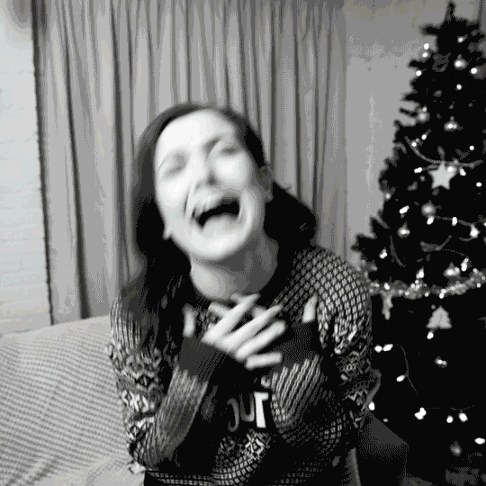 Video gif. A woman in a festive Christmas sweater throws her head back in laughter. Text, "Ha ha ha!"