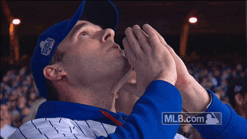 Video gif. A Chicago Cubs fan holds his palms together in prayer as he looks up toward the sky and whispers to himself.