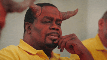 Video gif. A man wearing red makeup and prosthetic devil horns sits with his hand on his chin, contemplating something.