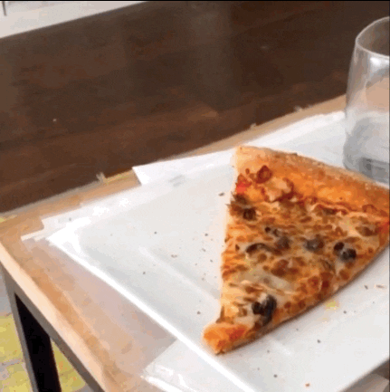 Video gif. A small dog stands up to a table on its hind legs and appears to dance around its edge, looking at a slice of pizza just out of reach.