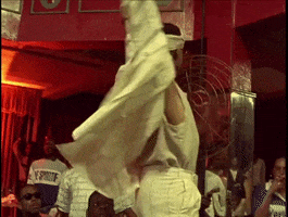 Movie gif. From the documentary Paris is Burning, LGBTQ icon Kim Pendavis raises his arms on the catwalk, showing off for the crowd with a pouty expression.