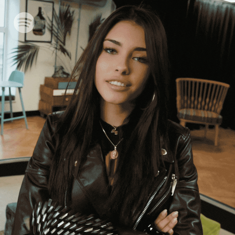 Celebrity gif. Wearing a leather jacket and studded gloves, Madison Beer smiles and then blows a kiss to us.