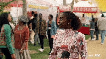 TV gif. Issa Rae on Insecure stands in the middle of a festival as people walk past her. She celebrates by herself, pumping both of her fists and smiling wide. 