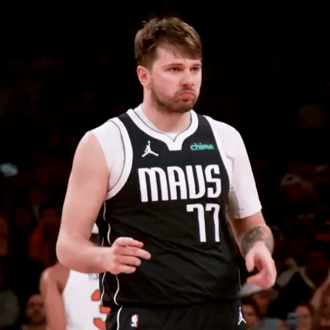 Sports gif. Luka Doncic of the Dallas Mavericks basketball team is walking on the court pointing his index fingers in an alternating forward motion with a slight pout on his face.