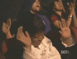 TV gif. A reverent woman closes her eyes in worship while clapping and raising her hands to God and swaying in her seat during BET Sunday Service. 