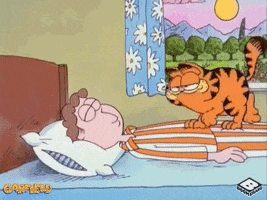 Cartoon gif. Garfield crawls across Jon as he sleeps, makes sure Jon is still sleeping, then dances on Jon's head. 