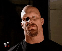 TV gif. Steve Austin glances down at us menacingly, then holds up a "Raw" microphone and says "What?" which appears as text.