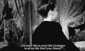 Celebrity gif. In black and white, Bette Davis as Maggie in The Man Who Came to Dinner turns around in front of the window as the snow falls outside. She smiles and says, “I've never felt so much like Christmas in all my life. Don’t you, Sherry?”
